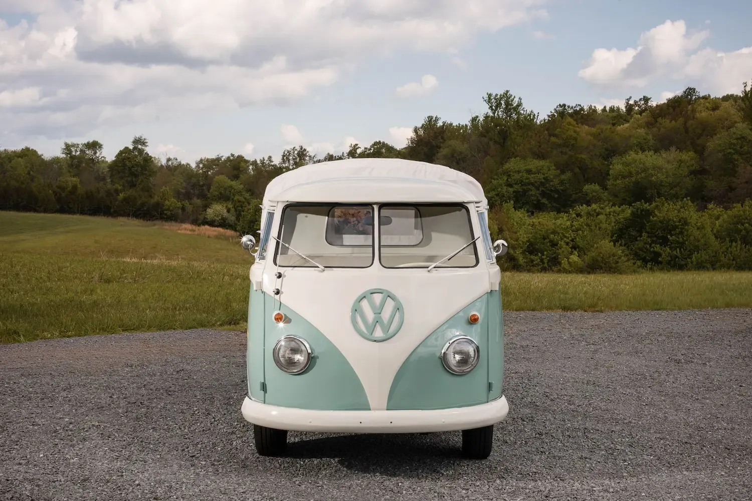 Rosi, a restored mint and white 1962 vintage truck, parked on a gravel road in front of trees and an open field.